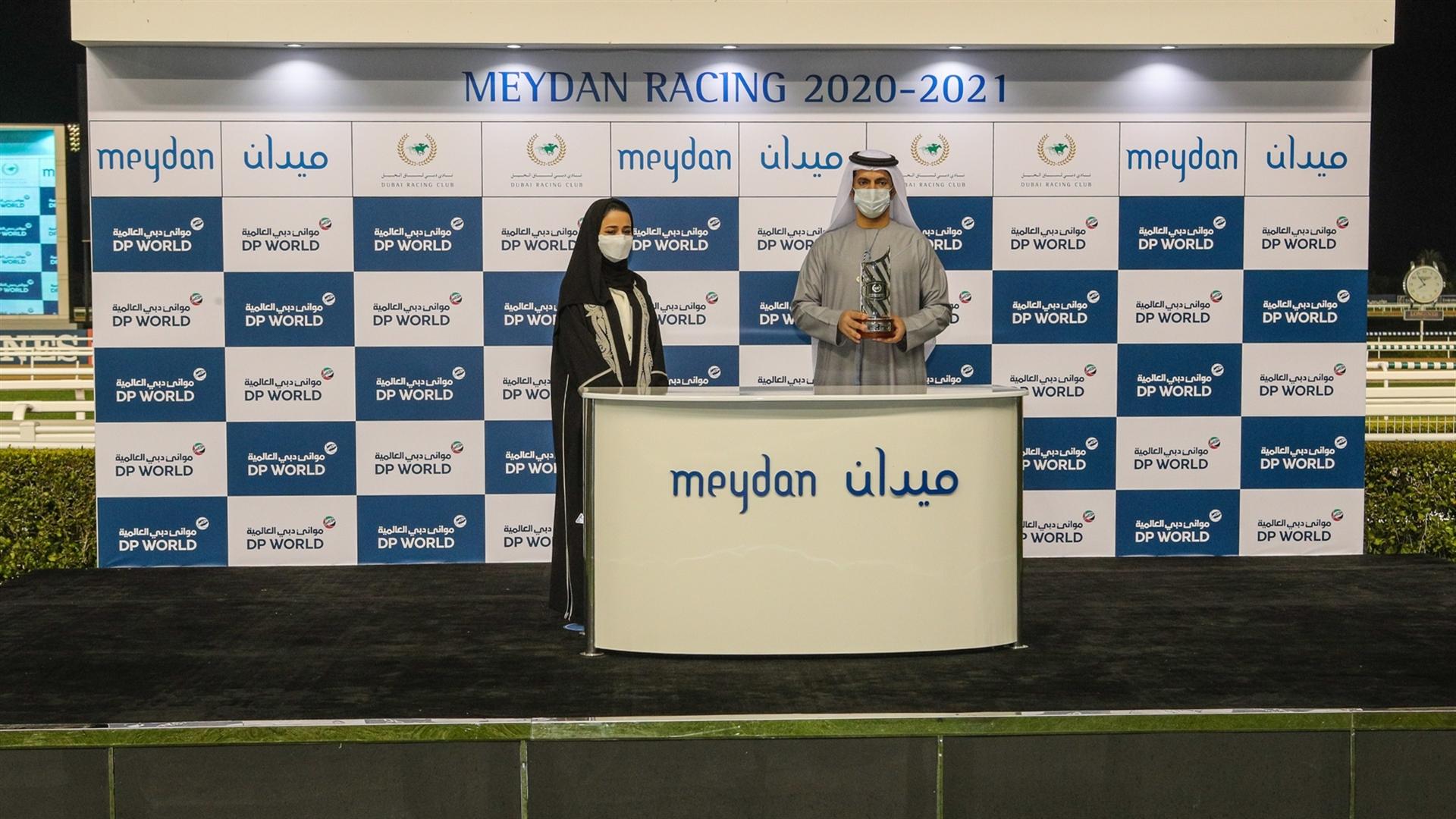 Saeed bin Suroor accepts the trophy for the JAFZA 2410m Handicap, from Ms. Ebtesam Ahmad Alkaabi, Head of Sales - JAFZA, on January 14, 2021.   (Credit: Dubai Racing Club)